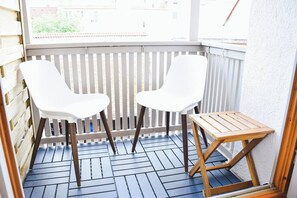 Een balkon met twee witte stoelen en een klein houten tafeltje.