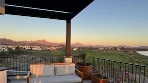 Ein Balkon mit einer Couch, einem Holztisch und Topfpflanzen.