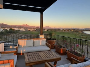A balcony with a sofa, a wooden table, and potted plants. - Beachfront Home & Mountain Views, and the Biggest Private Pool ( Andador Fisher Loreto)