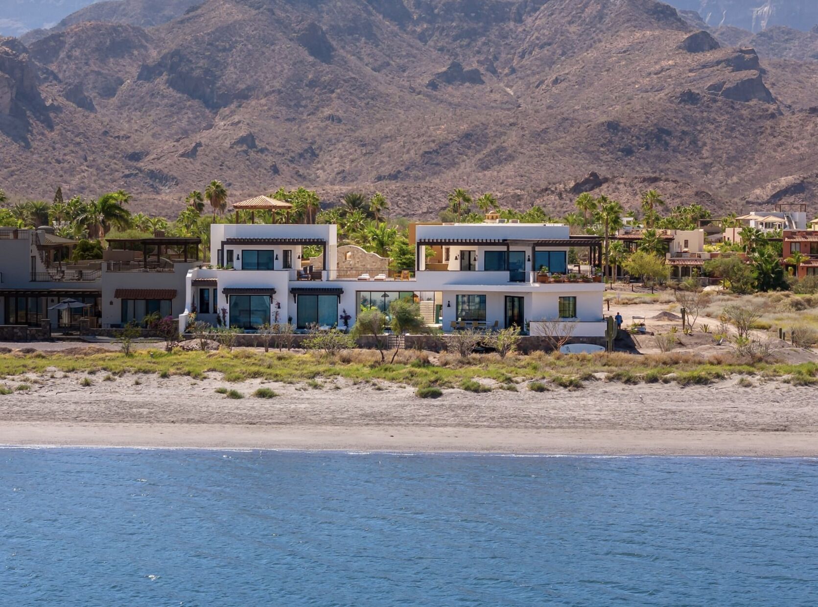 Una propiedad costera de arquitectura moderna, con vista a la playa y montañas al fondo.