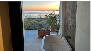 Ein Badezimmer mit Badewanne, Topfpflanzen und Meerblick bei Sonnenuntergang.