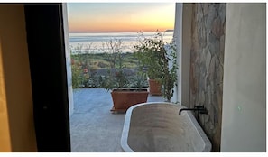 A bathroom with a bathtub, potted plants, and a view of the ocean at sunset. - Beachfront Home & Mountain Views, and the Biggest Private Pool ( Andador Fisher Loreto)