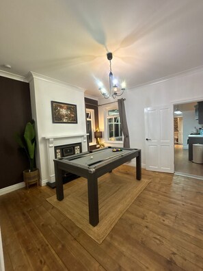 A pool table in a room with a fireplace, a chandelier, and a door leading to a kitchen. - Cope Corner (Walsall)