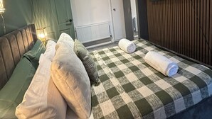 Une chambre d’hôtel avec un lit, des oreillers, une couverture à carreaux, un téléviseur fixé au mur et un luminaire au plafond.