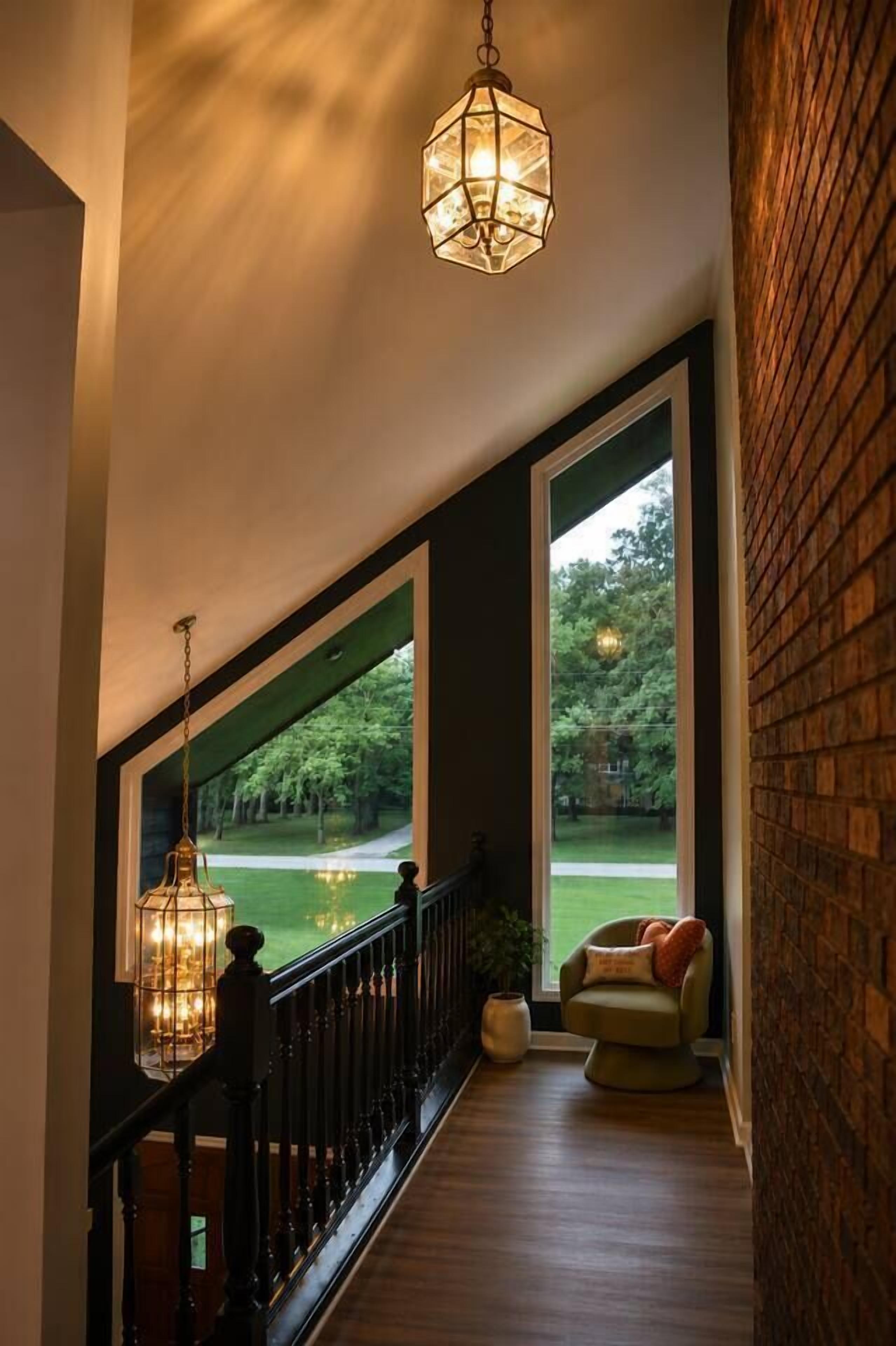 A spacious balcony with a railing, a hanging light fixture, and a view of a green landscape.