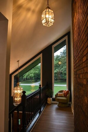 A spacious balcony with a railing, a hanging light fixture, and a view of a green landscape. - Sleeps 19 | 2 acres | Pets | MidCity | Space Camp (Huntsville)