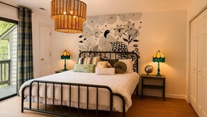 Una camera da letto con un letto, due comodini, una lampada a sospensione, un arazzo a parete e una porta.