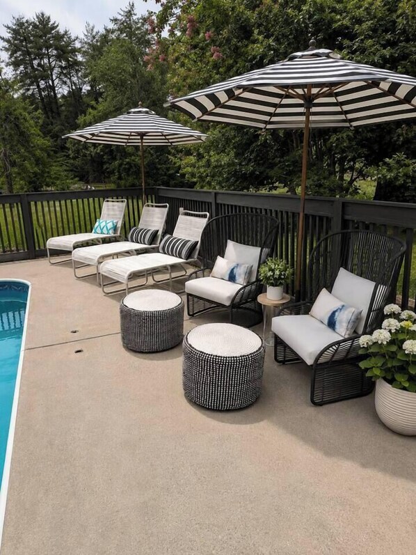 Een zwembadterras met ligbedden, gestreepte parasols en ronde poefs.