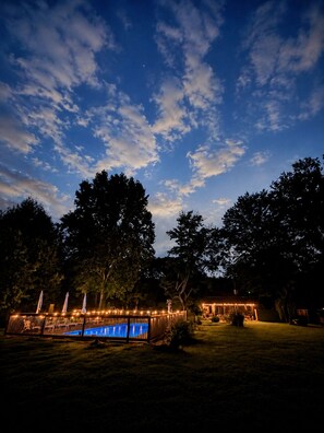 A nighttime outdoor area with a pool, umbrellas, and a building with lights. - Sleeps 19 | 2 acres | Pets | MidCity | Space Camp (Huntsville)