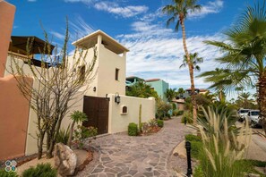 A pathway leading to a building with a flat roof and a door, surrounded by palm trees and a clear sky. - Pleasant Home Close to Community Pool and Wine bar (  Loreto)