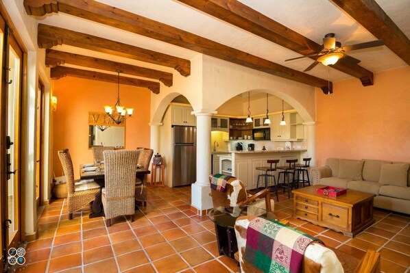 Un salón espacioso con una mesa de comedor, sillas de mimbre, un sofá y un perro.