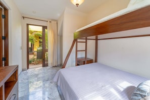 Un dormitorio con una litera, cabecera de madera, una mesita de noche pequeña y vistas a un jardín por una puerta abierta.