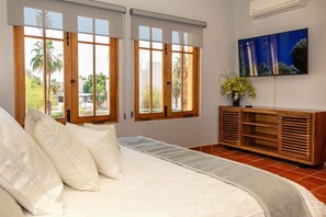 Ein Schlafzimmer mit einem Bett, zwei Fenstern mit Jalousien, einem Fernseher an der Wand und einem Holzschrank.