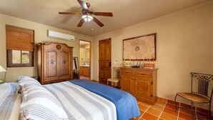 Ein Schlafzimmer mit einem Bett, einem Holzschrank, einem Spiegel, einem Deckenventilator und einem Sessel.