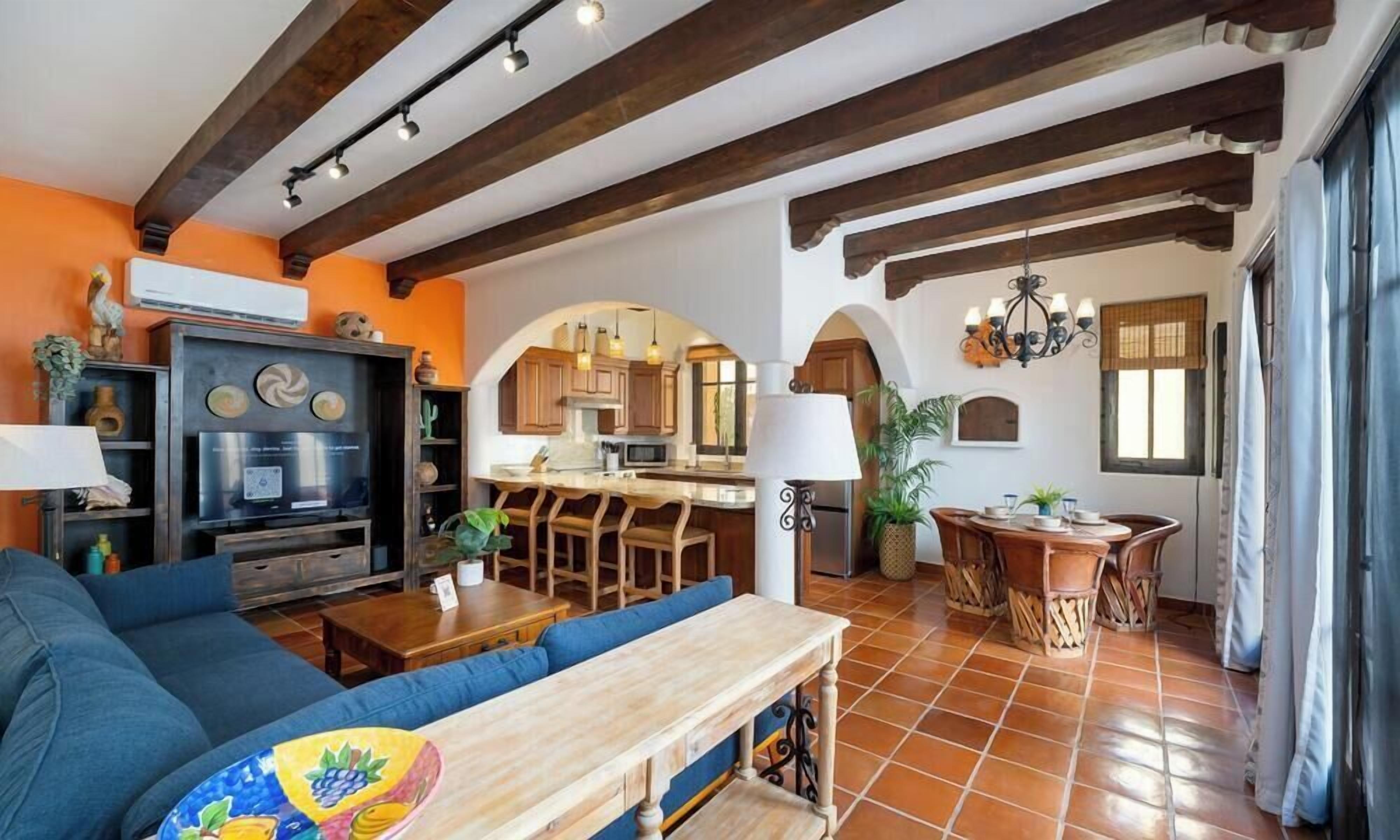 Una sala de estar con sofá, una mesa de centro de madera y una cocina con alacenas de madera y una mesa de comedor.