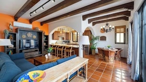 Una sala de estar con sofá, una mesa de centro de madera y una cocina con alacenas de madera y una mesa de comedor.