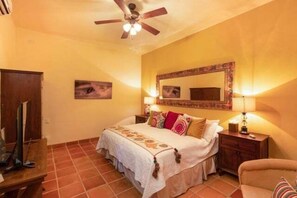 A bedroom with a bed, a ceiling fan, a bedside table with a lamp, a chair, and a wooden wardrobe. - Cozy Home a few Steps From Community Pool (  Loreto)