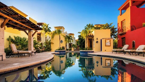 A pool area with lounge chairs, a reflection pool, and a building with a red facade. - Cozy Home a few Steps From Community Pool (  Loreto)