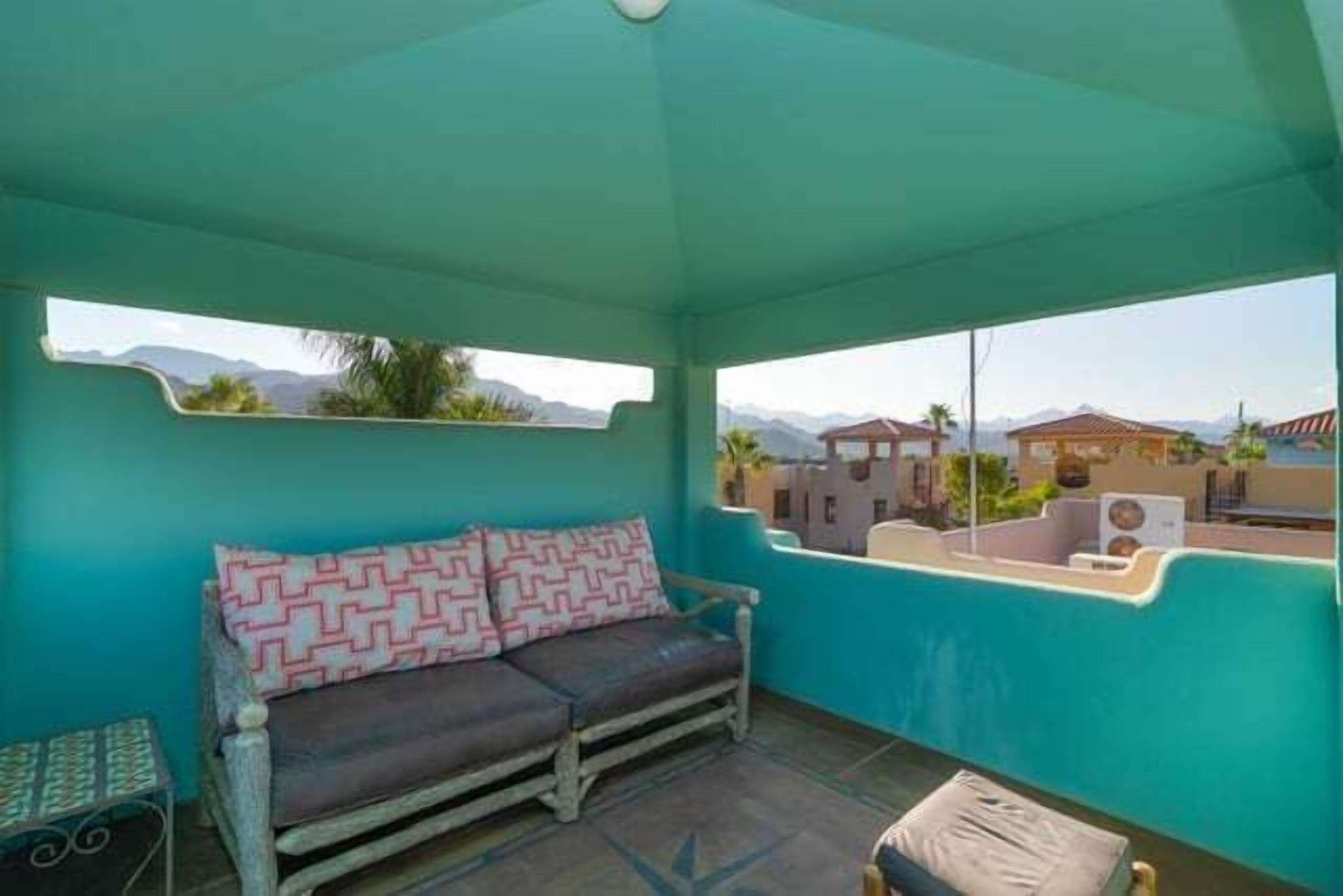 Une pièce avec un mur de couleur turquoise, un canapé orné de coussins à motifs, une petite table et une vue sur des bâtiments et des montagnes.
