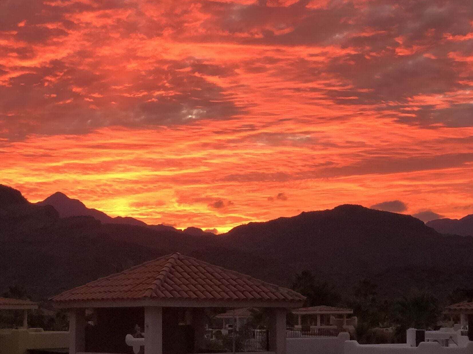 A sunset over mountains with a small building in the foreground.