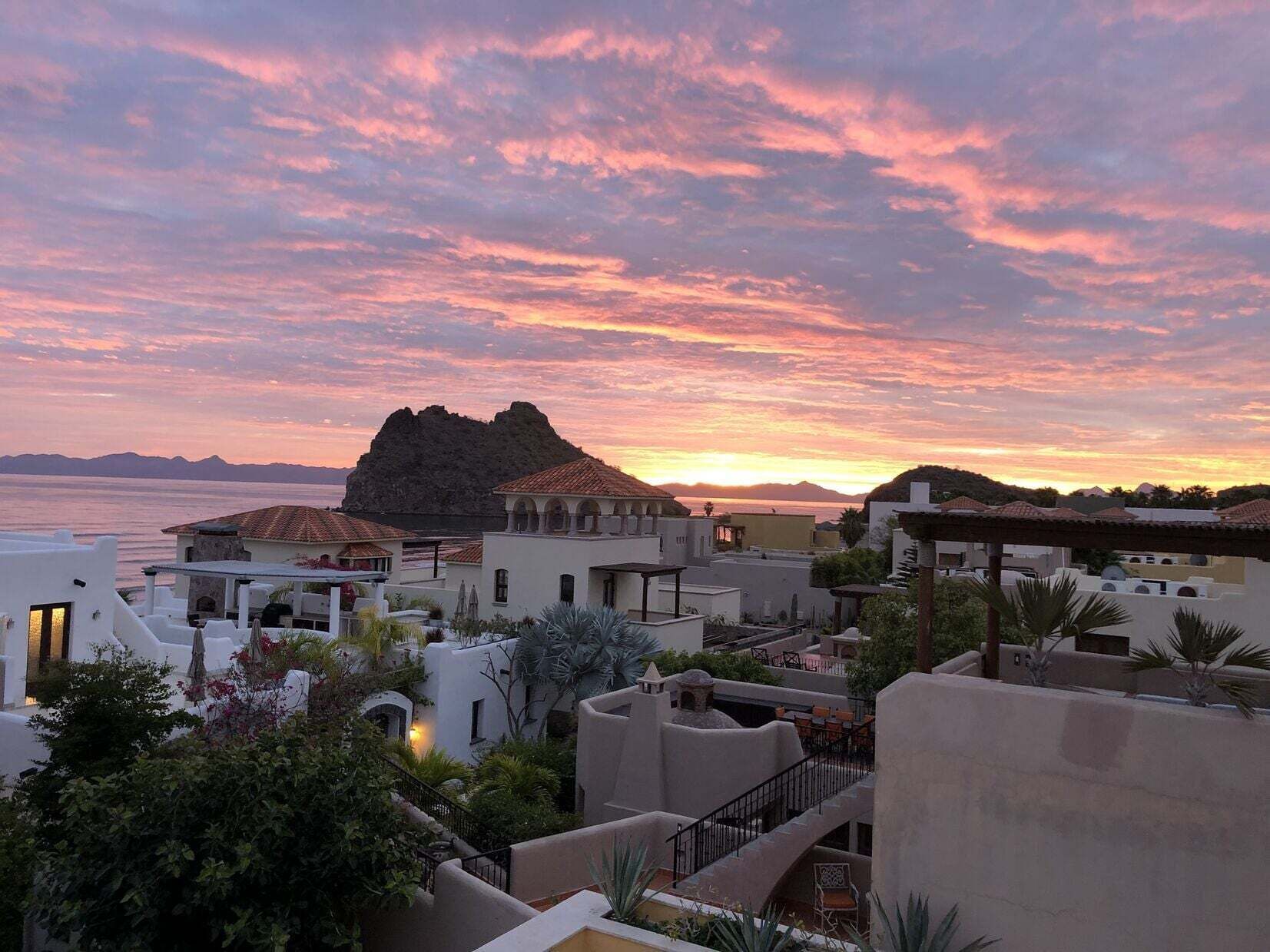 A coastal town with buildings, a prominent rock formation, and a sunset view.