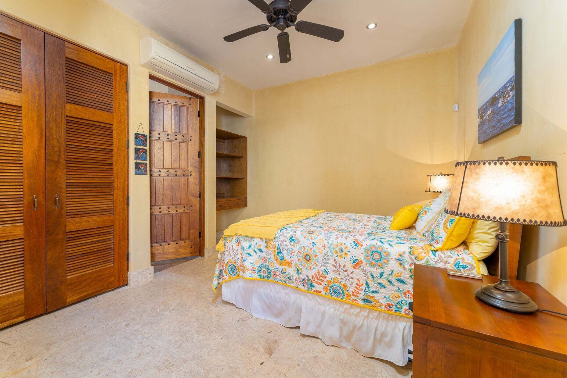 Une chambre à coucher comprenant un lit, un bureau, une lampe, un ventilateur de plafond et une armoire.