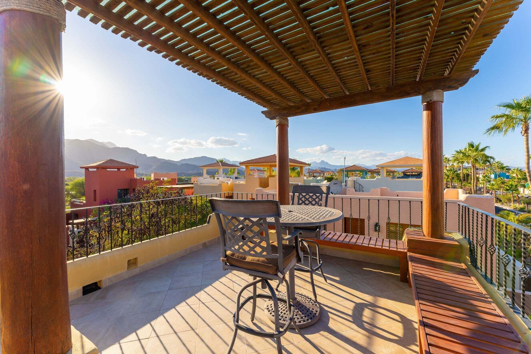 Un espacio al aire libre techado con una mesa y sillas, y vistas a edificios y montañas al fondo.