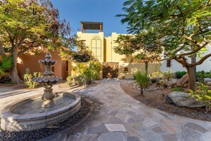 Un patio con una fuente de piedra, cactus y un edificio con una pérgola.