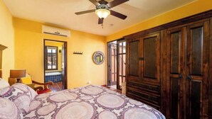 Une chambre à coucher comprenant un lit, un ventilateur de plafond, un appareil de climatisation, une armoire en bois et une fenêtre donnant sur un paysage agréable.