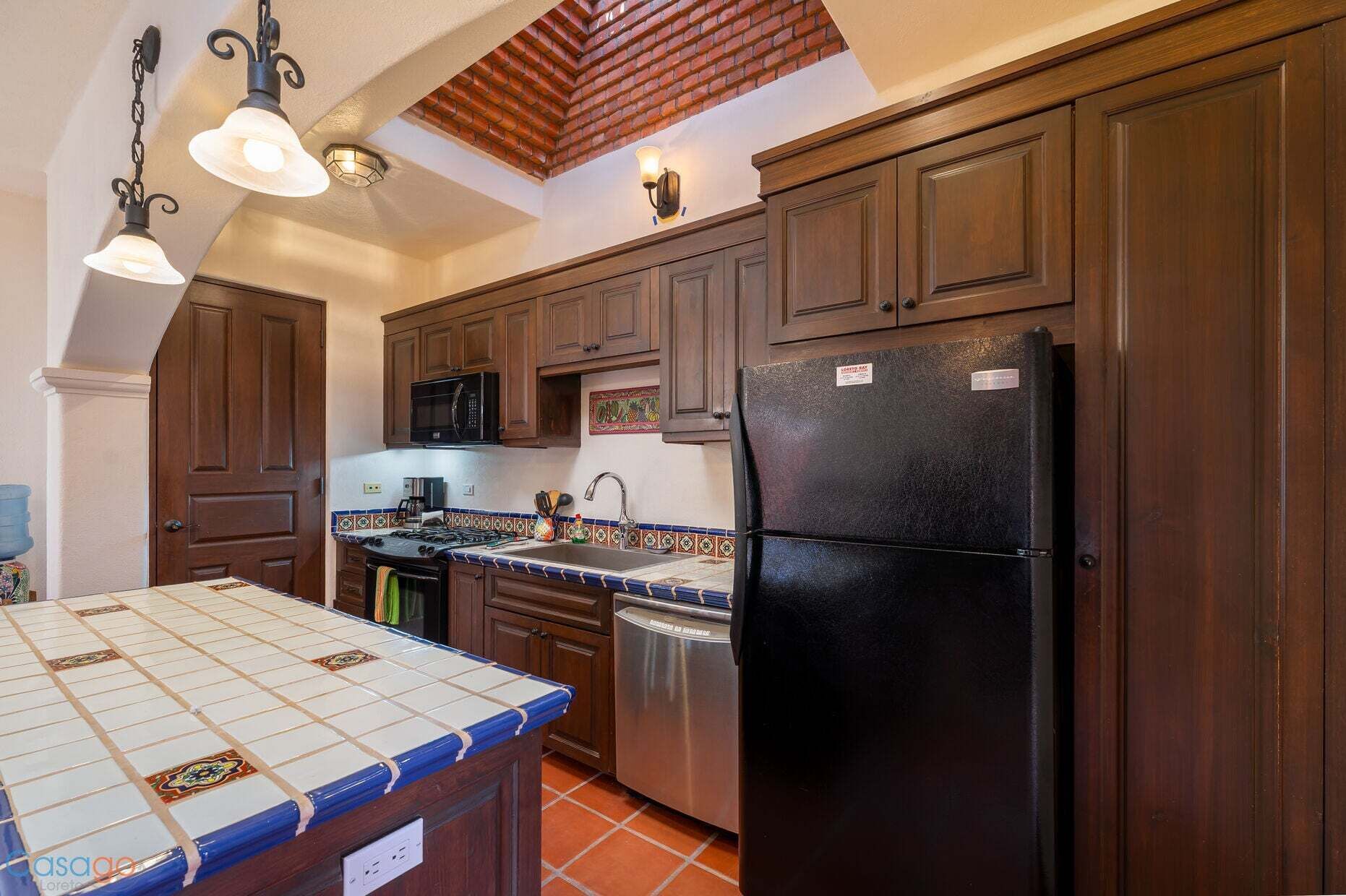 Una cocina con armarios de madera, un refrigerador negro, una estufa y un microondas.