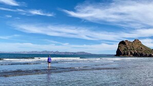 A beach with a person walking towards the water, a rocky outcrop, and distant mountains under a clear sky. - Newly Renovated Home- 5 Steps From LAP Pool (  Loreto)