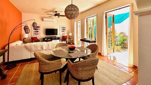 A modern living room with a round glass table, woven chairs, a ceiling fan, and a large window with a view of a garden. - Newly Renovated Home- 5 Steps From LAP Pool (  Loreto)