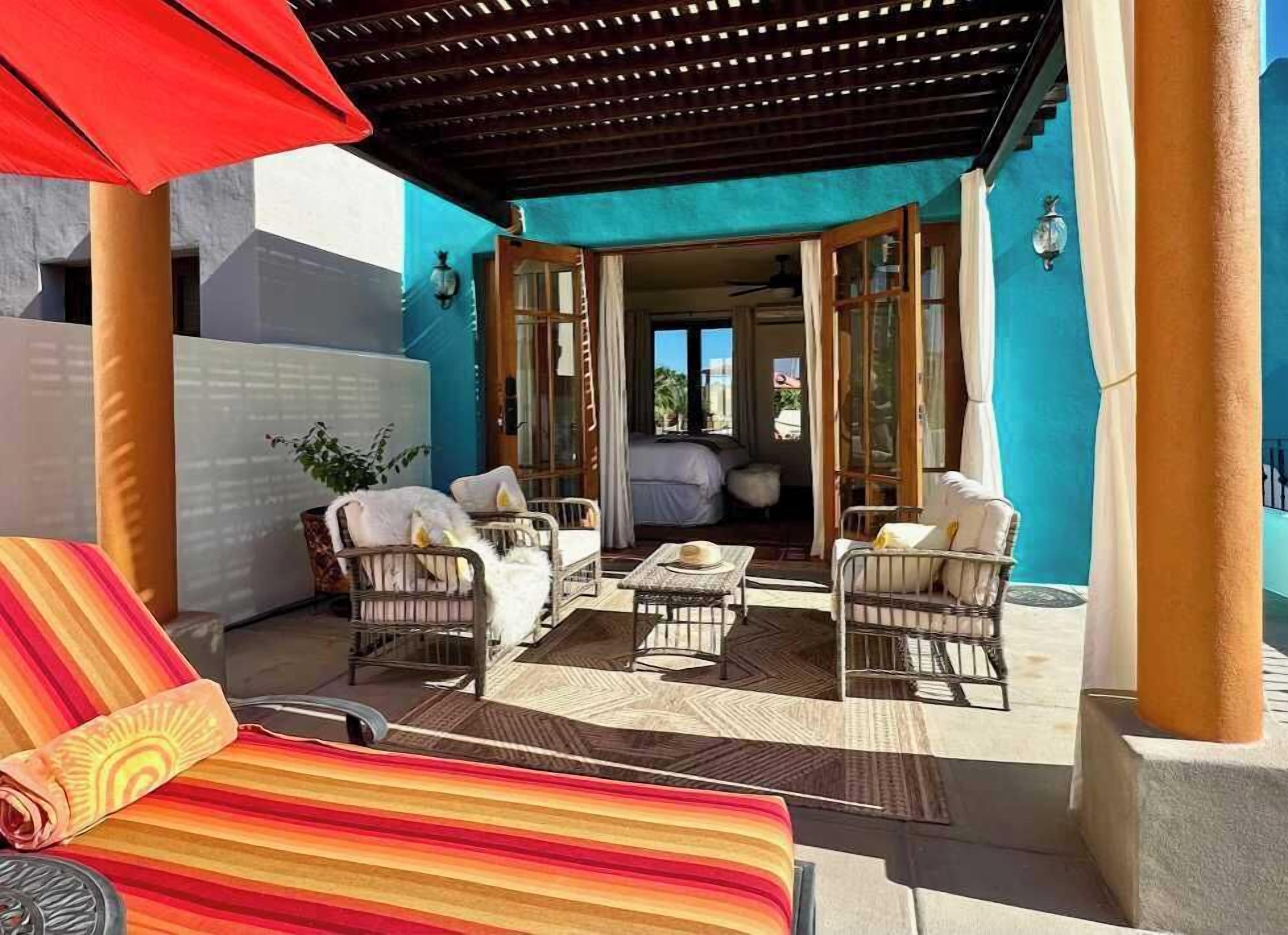 Un patio al aire libre con mobiliario de mimbre, una toalla a rayas y un paraguas rojo.