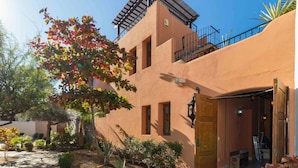 Ein Gebäude mit einem gepflasterten Innenhof, einer Holztür und einem kleinen Garten mit verschiedenen Pflanzen.