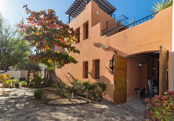 A building with a stone-paved courtyard, a wooden door, and a small garden with various plants. - Beautiful Home With Private Pool Amazing Views! (  Loreto)