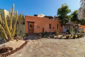 Un edificio con fachada de estuco, una puerta y un pequeño jardín con cactus y rocas.