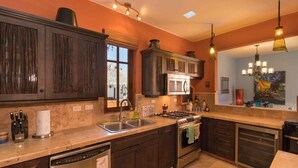 A kitchen with dark wooden cabinets, a stainless steel range, a dishwasher, and a large window with a view of a thatched roof structure. - Beautiful Home With Private Pool Amazing Views! (  Loreto)