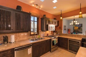 A kitchen with dark wooden cabinets, a stainless steel range, a dishwasher, and a large window with a view of a thatched roof structure. - Beautiful Home With Private Pool Amazing Views! (  Loreto)