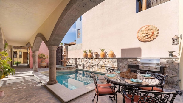 A poolside area with a stone wall, a grill, and a dining table with chairs. - Home With Stunning Ocean View and Breathtaking Sights of the Sierra La Giganta (  Loreto)
