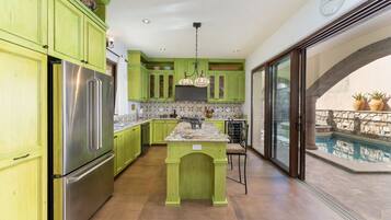 Cocina con armarios verdes, un refrigerador de acero inoxidable, salpicadero de azulejos y vistas a una piscina al aire libre.