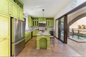 A kitchen with green cabinets, a stainless steel refrigerator, a tiled backsplash, and a view of an outdoor swimming pool. - Home With Stunning Ocean View and Breathtaking Sights of the Sierra La Giganta (  Loreto)