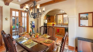 Un comedor con una mesa de madera dispuesta para una comida, una araña y vistas a la cocina.