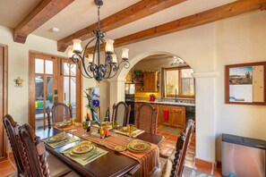 A dining area with a wooden table set for a meal, a chandelier, and a view into the kitchen. - Less Than 5 Minutes From the Beach and Community Pool! ( Col. Nopolo Loreto)
