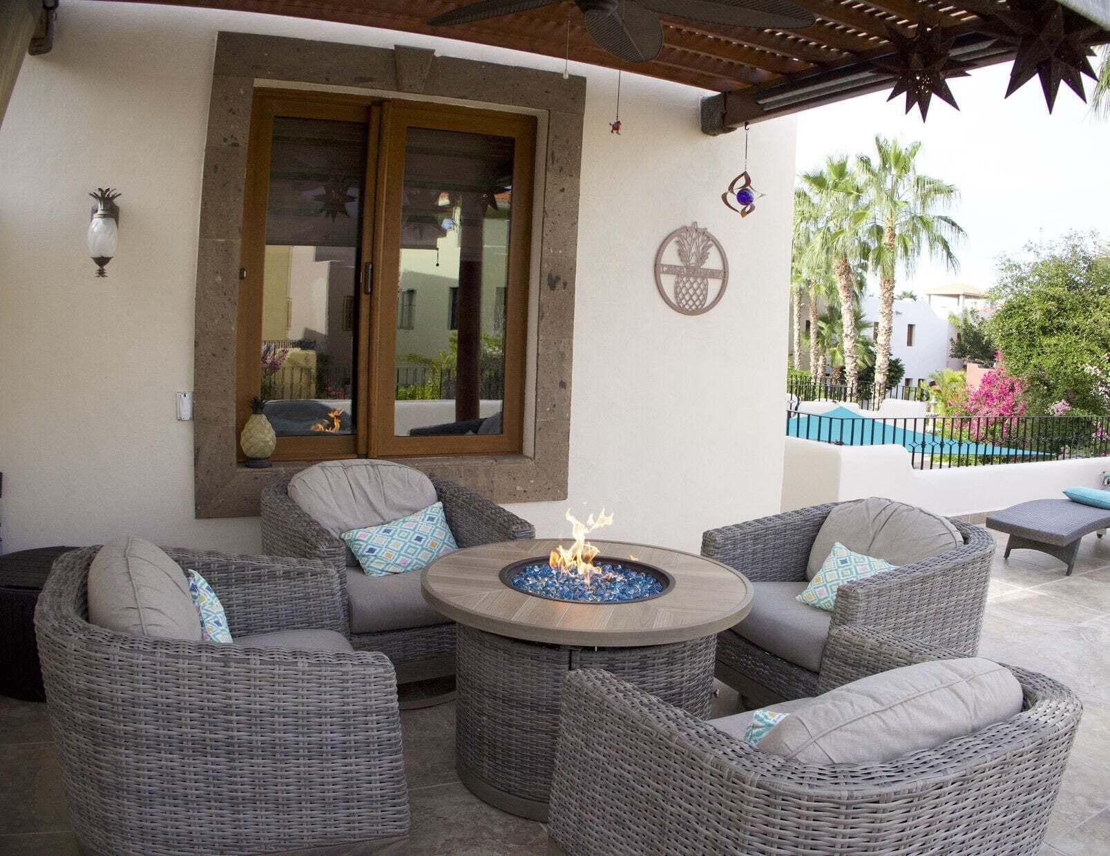 Un espace patio aménagé avec des meubles en osier, un foyer extérieur et une vue sur une piscine et des palmiers.