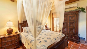 Un dormitorio con una cama con dosel, mesitas de noche de madera, una lámpara de noche y un armario de madera.