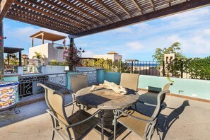 Un patio exterior con una mesa redonda y sillas, una pérgola encima y vista al mar.
