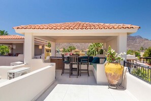 Un espace extérieur abrité, aménagé avec une table de patio, des chaises et un grand vase rempli de fleurs.