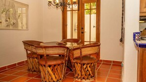 A dining area with a round table and four chairs, a chandelier, a wooden door with glass panels, and a tiled floor. - Ideal Home, Perfect Location in Loreto Bay, Steps From the Beach With Private Pool. By Casago (  Loreto)