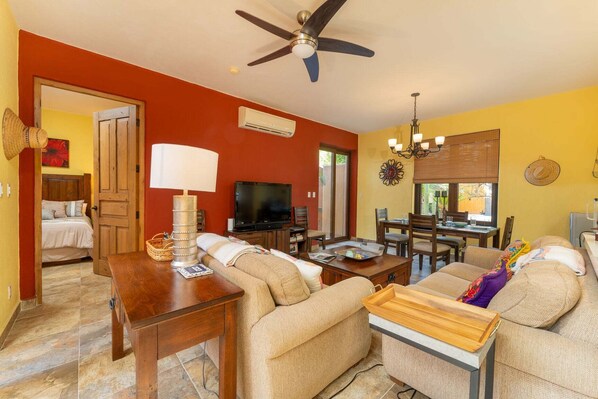 A living room with a sofa, TV, dining table, and ceiling fan.