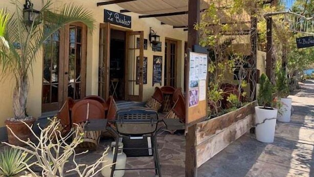 A covered outdoor seating area with tables and chairs, a sign reading "Le Bistro," and potted plants. - Wonderful Home Next to the Community Pool (  Loreto)